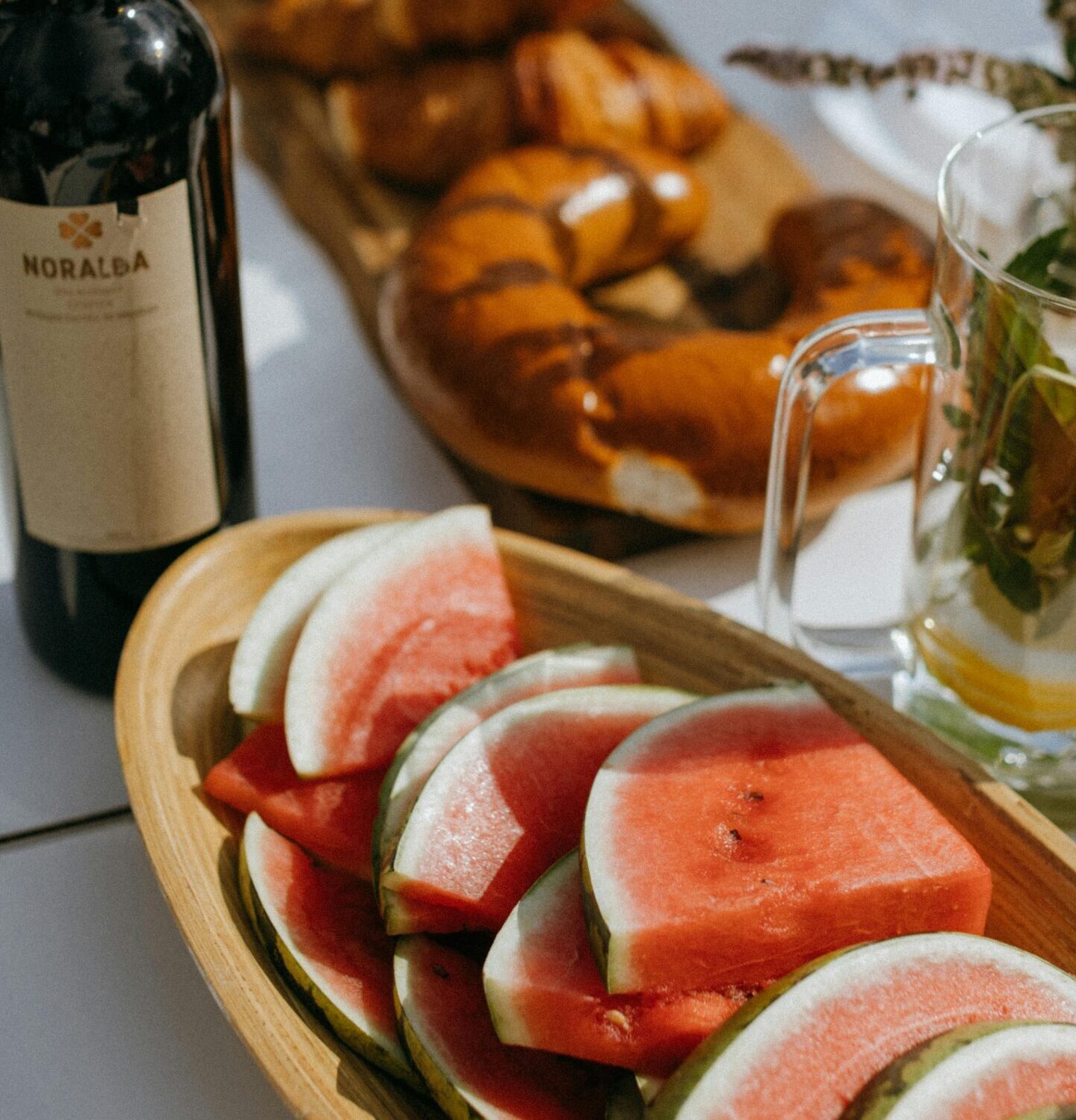 Celebrate summer outdoors with wine, fresh watermelon, and delicious pastries on a picnic table.